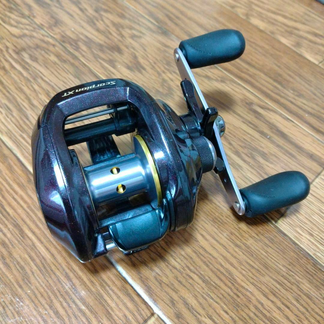 Shimano '09 Scorpion XT 1500 baitcasting fishing reel on a wood floor, showing the spool and dual handle from an angled view.