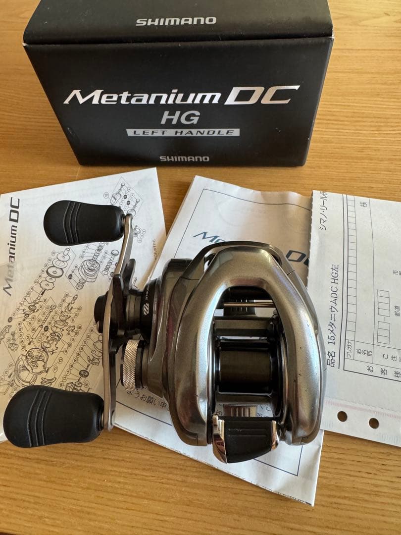 Shimano 15 Metanium DC HG left-handle fishing reel on top of manuals with its box behind.