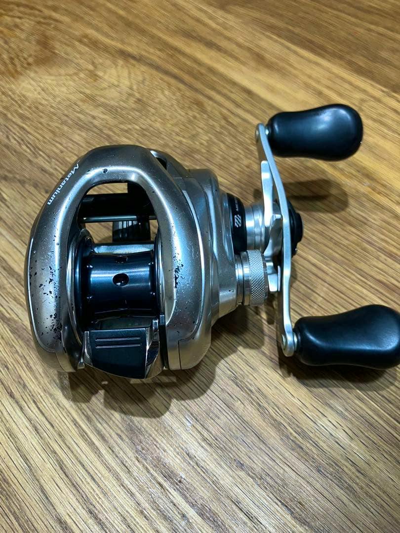 Shimano 16 Metanium MGL baitcasting reel on a wooden surface, top-front view showing scuffs and wear.