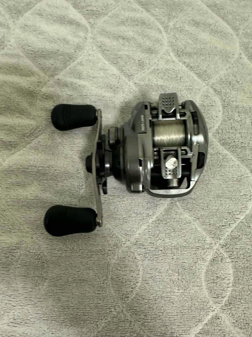 A SHIMANO baitcasting reel body lying on a textured towel, shown from a side angle with the handle and spool visible.