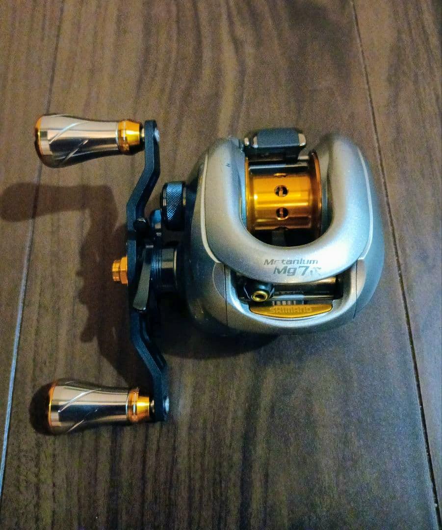Top-down photo of a SHIMANO Metanium Mg7 baitcasting reel showing the handle and spool on a wooden surface.