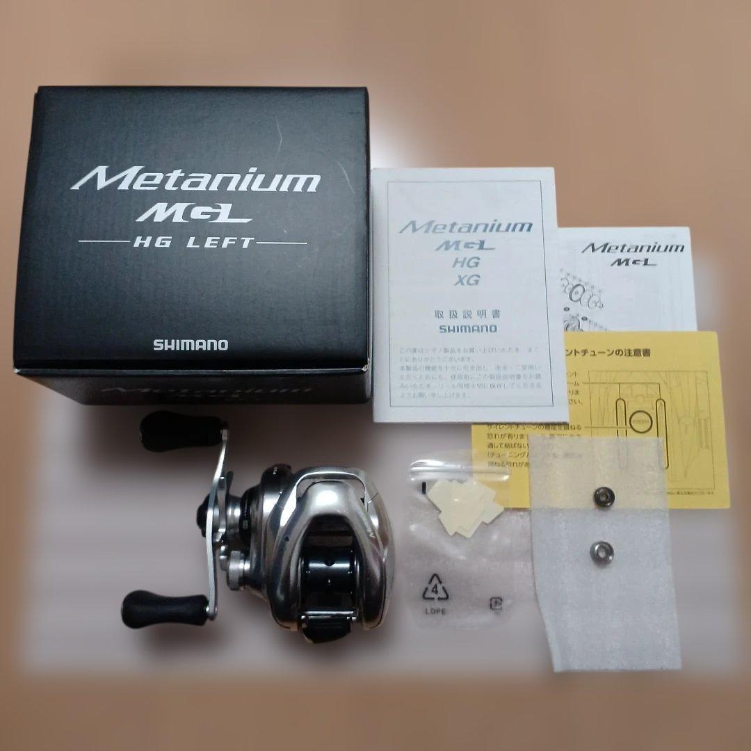 Top-down photo of a Shimano Metanium MGL HG LEFT baitcasting reel shown with its box, manuals, and small spare parts.