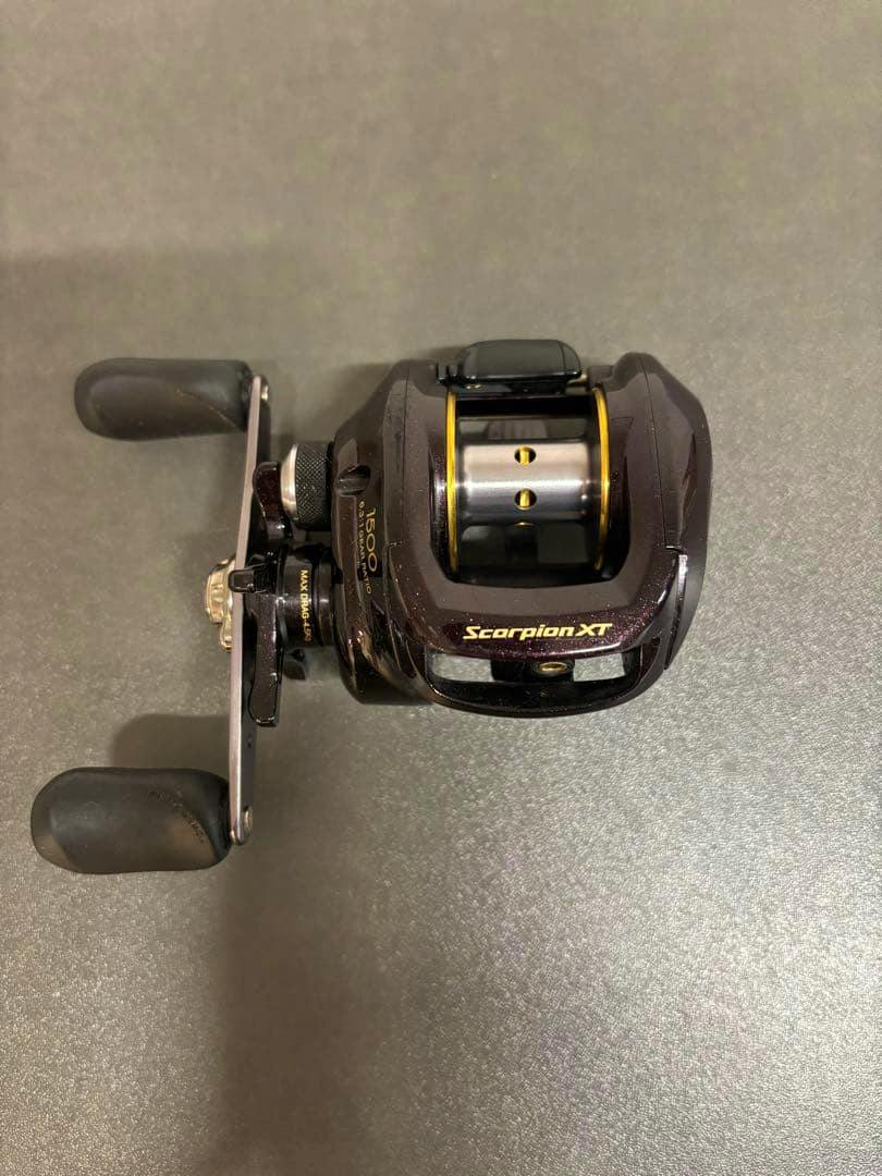 Top-down photo of the SHIMANO Scorpion XT 1500 baitcasting reel showing the spool, handle, and Scorpion XT logo on a gray surface.