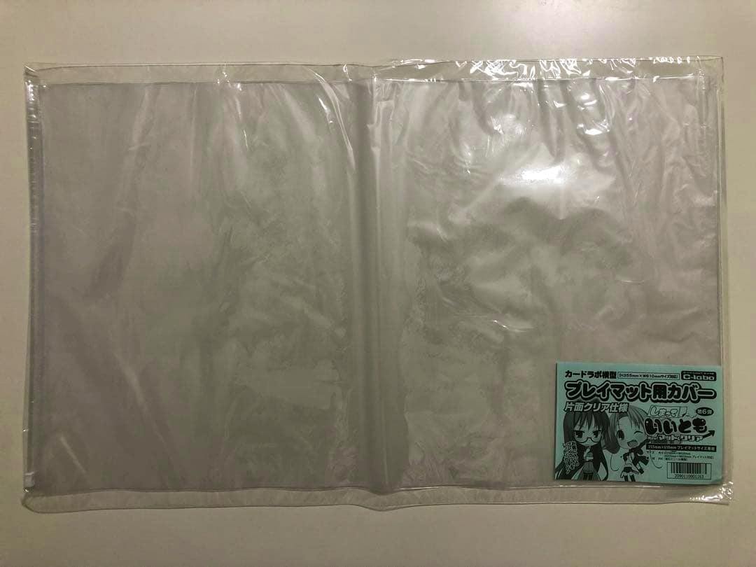Horizontal clear plastic playmat cover laid flat with a small product label at the lower right.
