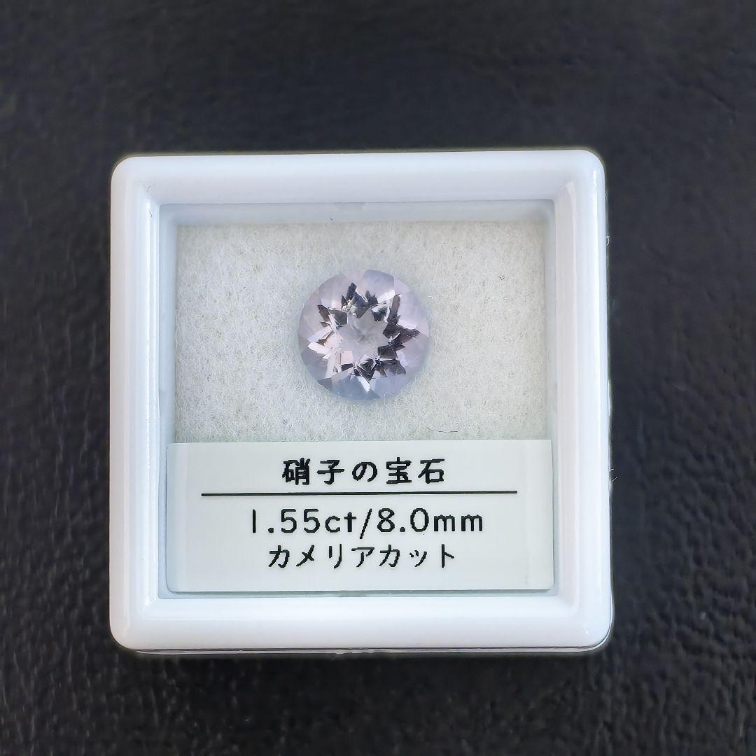 A pale purple camellia-cut glass gemstone displayed in a small white box with a label showing its weight and size.