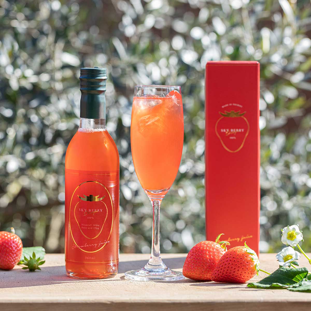 A bottle of Sky Berry Drops 360ml strawberry juice shown with its red box, a filled glass, and fresh strawberries.