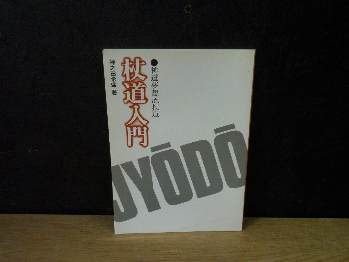 Front cover of the book '新道夢想流杖道 杖道入門' standing on a wooden surface against a dark background.