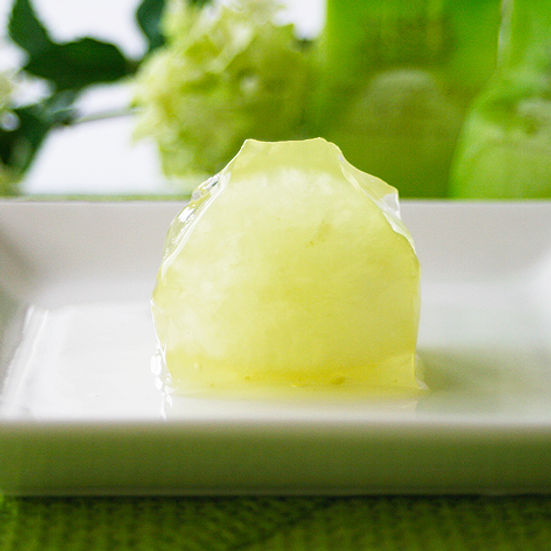 A single pale green Shine Muscat grape jelly piece placed on a small white rectangular plate.