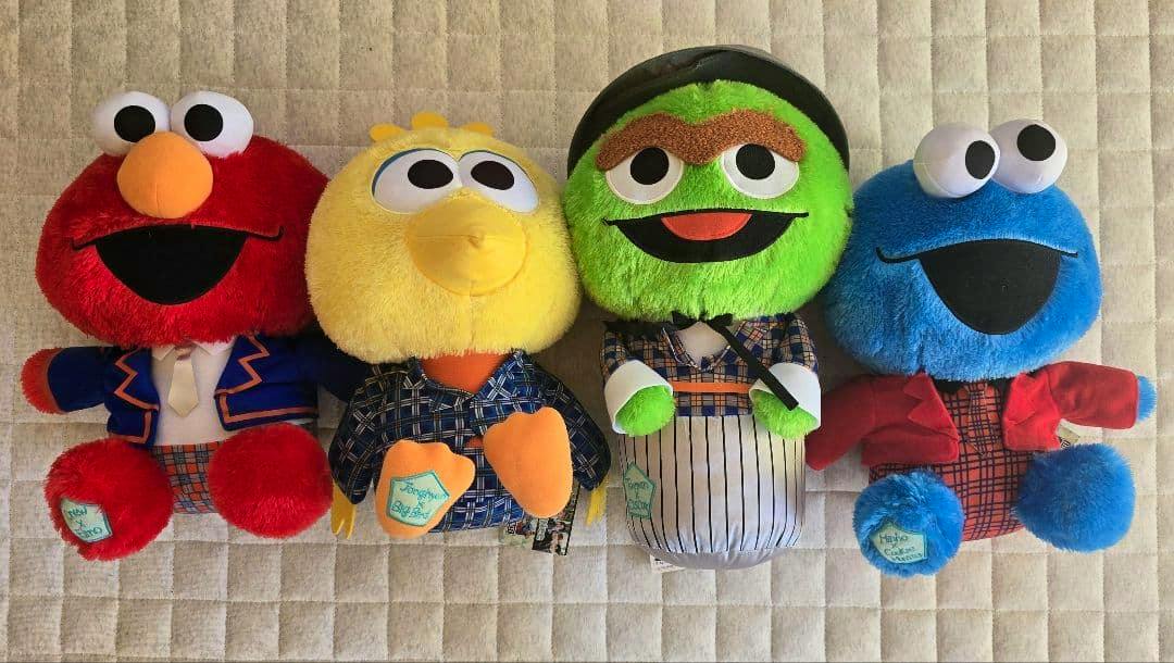 Four Sesame Street plush toys from the SHINee collaboration arranged side by side on a quilted surface.