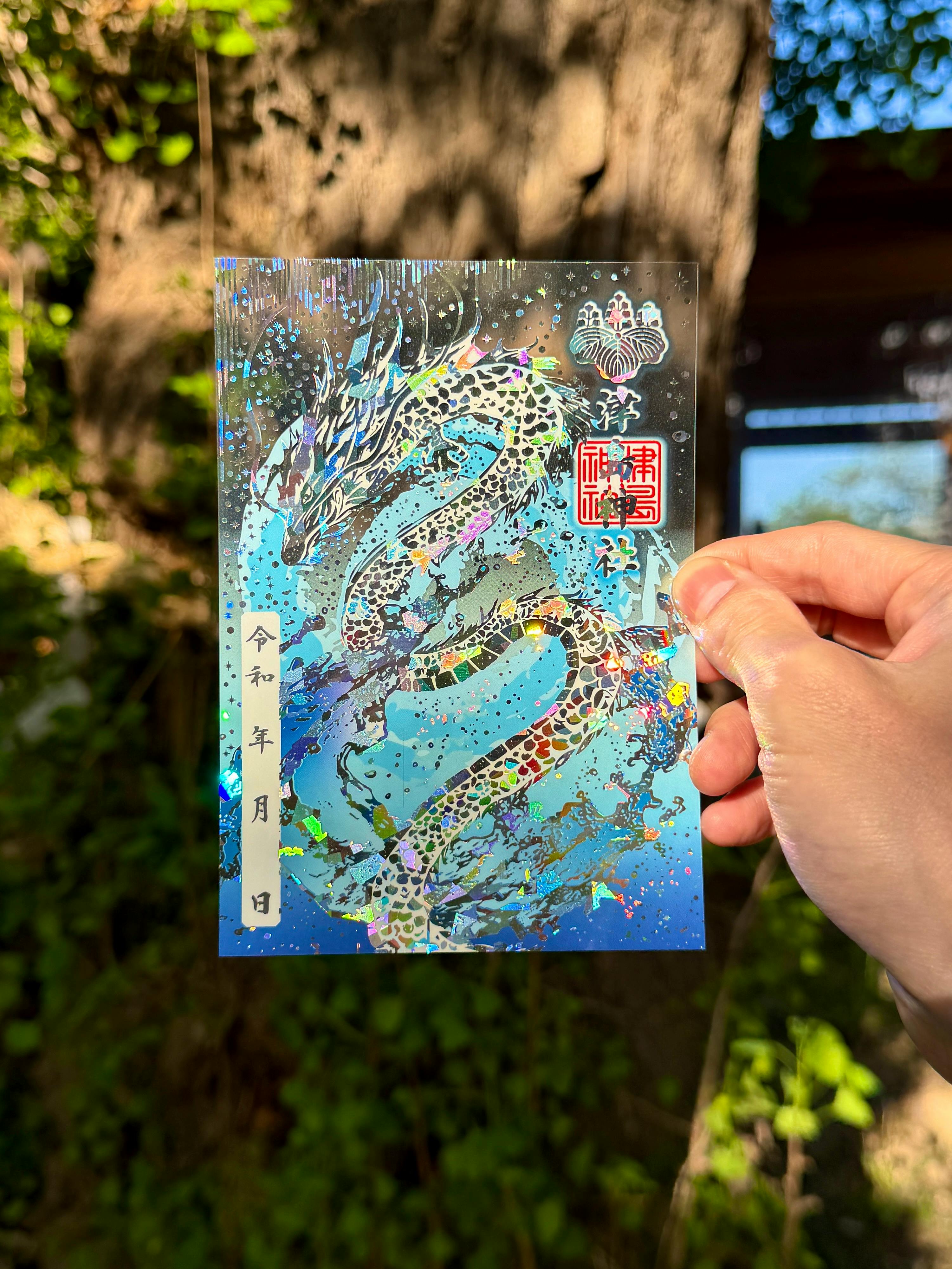A holographic blue dragon goshuin art print with special hologram foil held by a hand against an outdoor background.