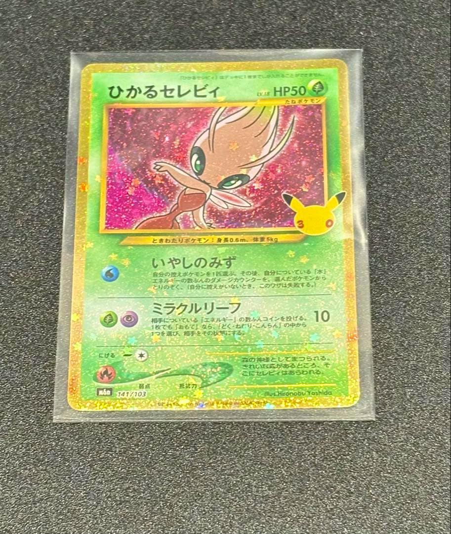 Photograph of the front of the ひかるセレビィ trading card in a clear sleeve showing holographic art and Japanese text on a black textured background.