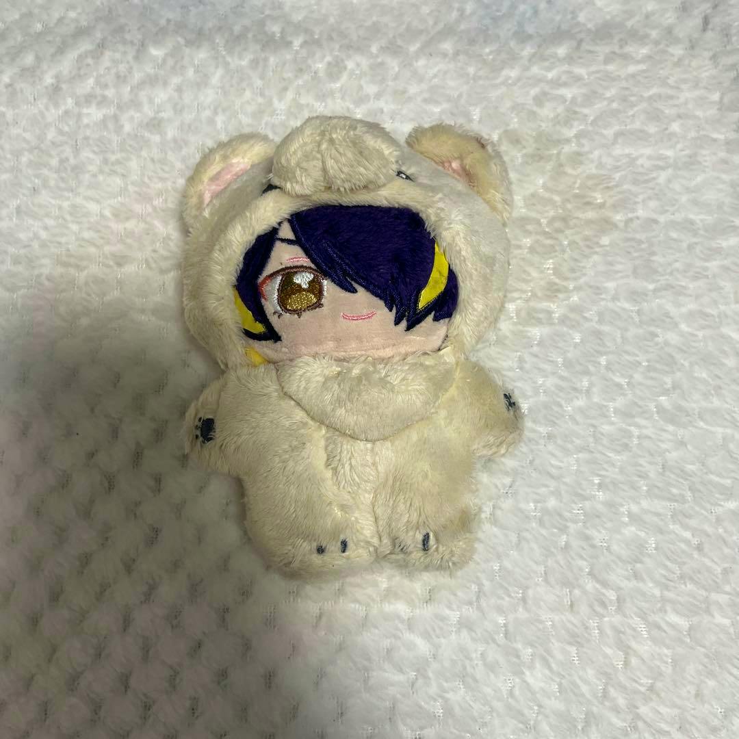 Front view of the 仙石忍 plush (ぬいぐるみ) wearing a light-colored bear costume, showing the character's embroidered face and hood.