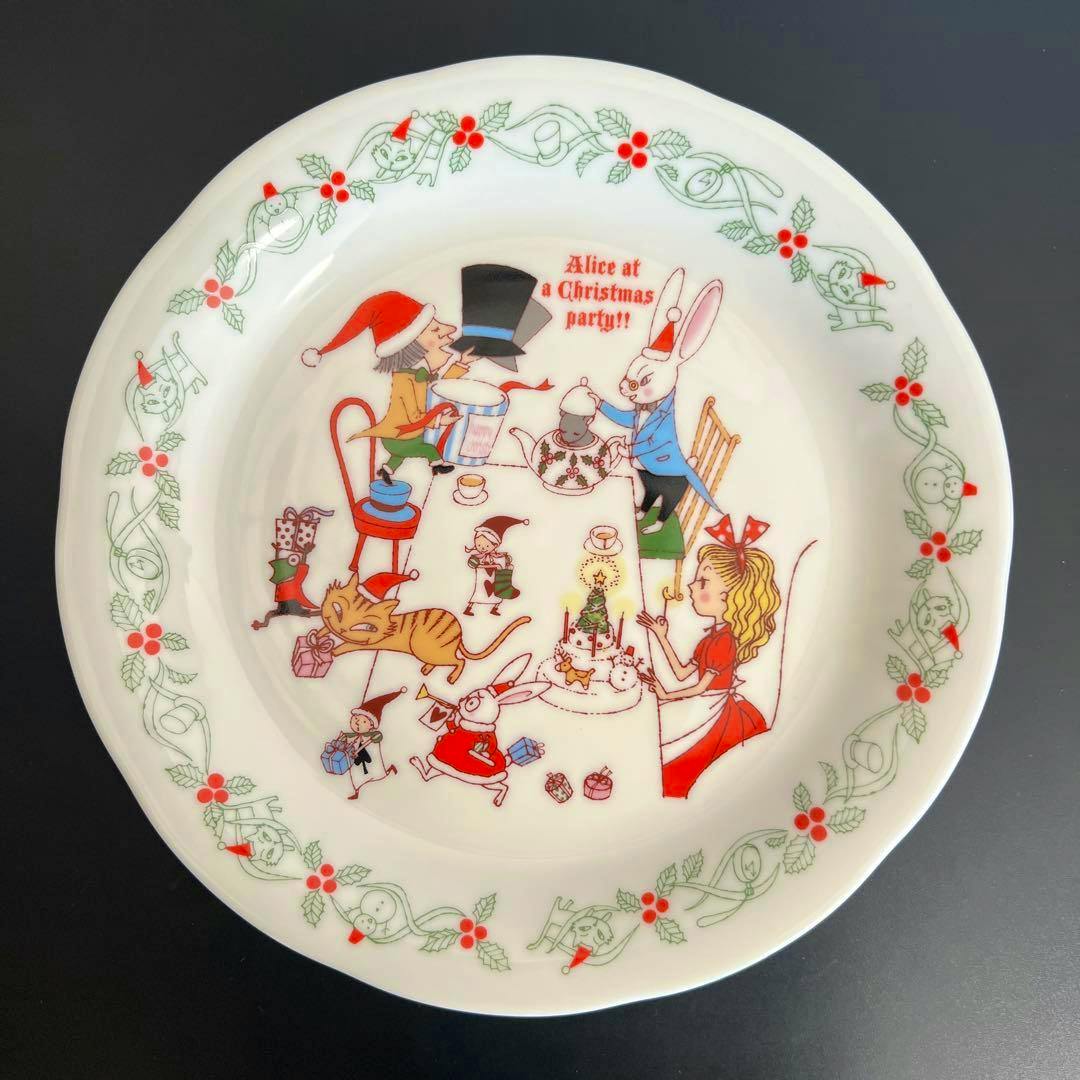 Top view of a ceramic plate showing a Shinzi Katoh Alice Christmas tea-party illustration with a holly-decorated rim.