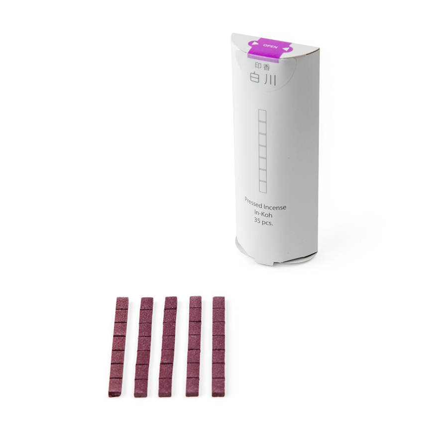A white cylindrical package of pressed incense and five purple pressed incense sticks displayed below.