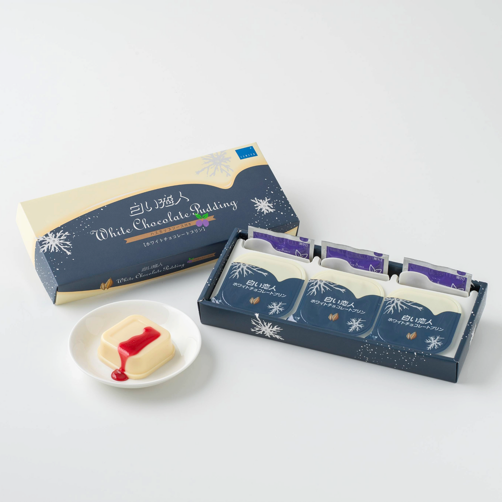 Boxed set of three white chocolate puddings with one pudding served on a small plate topped with red sauce.