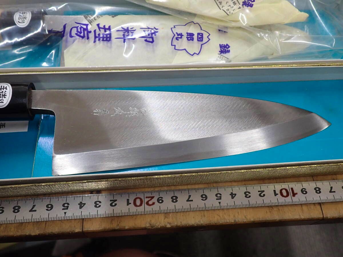 A Japanese chef knife blade and partial handle shown inside its box with a measuring tape.