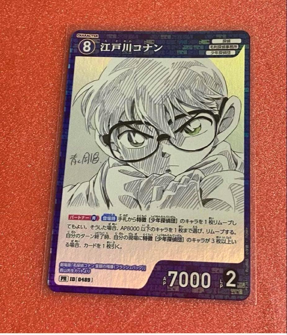 Photograph of a trading card for 江戸川コナン (Detective Conan) showing a sketch-style portrait, Japanese text, and stats AP 7000 and LP 2 on a red textured background.