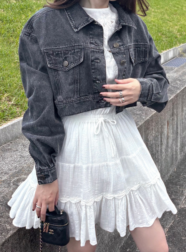 Model wearing the short-length denim jacket over a white dress, showing the jacket's front and sleeve details.