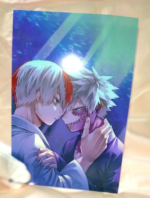 Photograph of the clear postcard showing two illustrated characters facing each other, placed on beige fabric with a glare on the card.