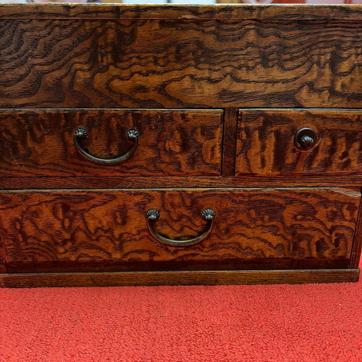 Close-up of a wooden small chest with two drawers and metal handles showing a curly wood grain on a red carpet.