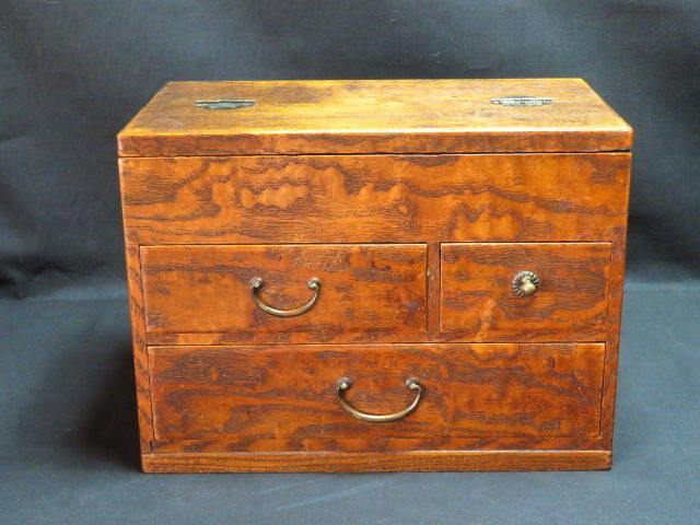 Closed wooden sewing box showing wood grain and metal drawer handles on a dark background.