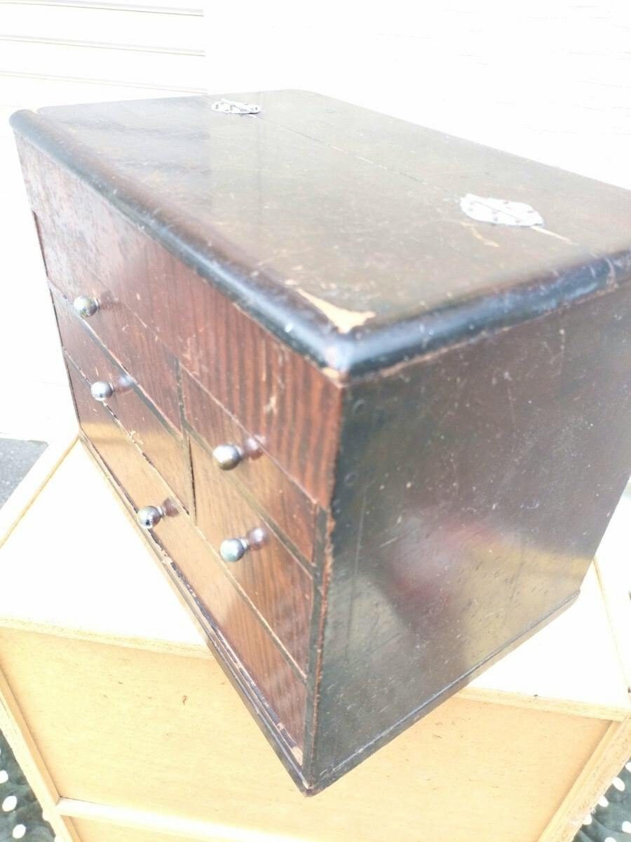 Angled photo of a wooden small-drawer storage chest with five drawers, metal knobs, and a worn finish.