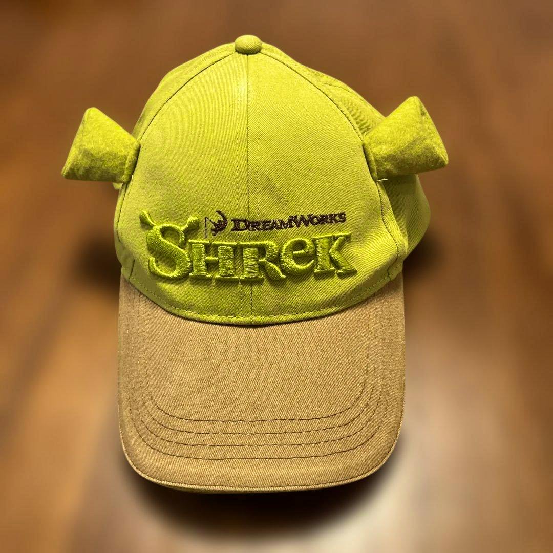Front view of the Shrek Universal Studios Singapore baseball cap showing embroidered "Shrek" logo, DreamWorks text, small ear details, and a tan brim.