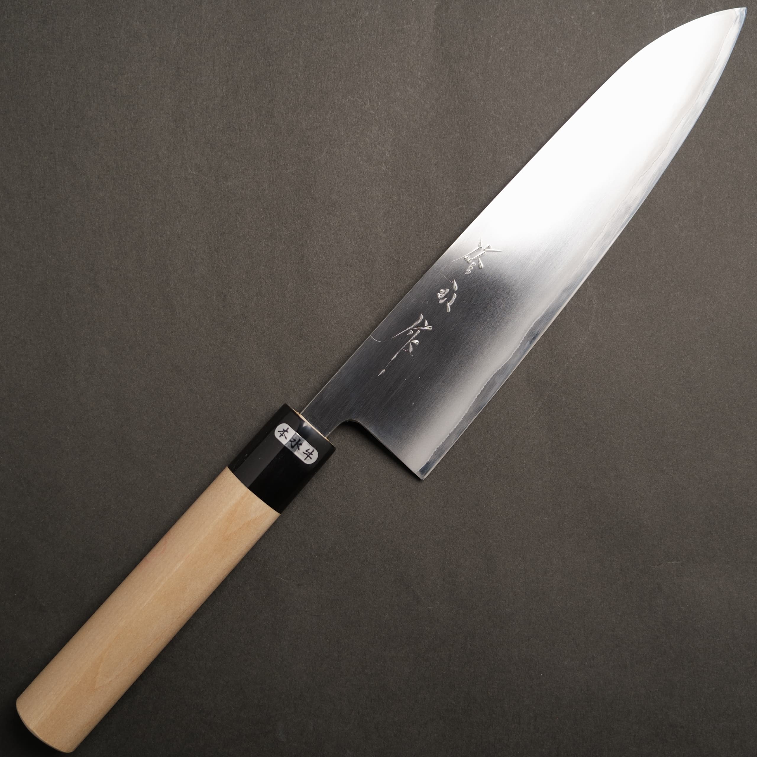 A 210mm Japanese chef knife with a polished stainless blade and a water-buffalo-style handle shown on a dark background.