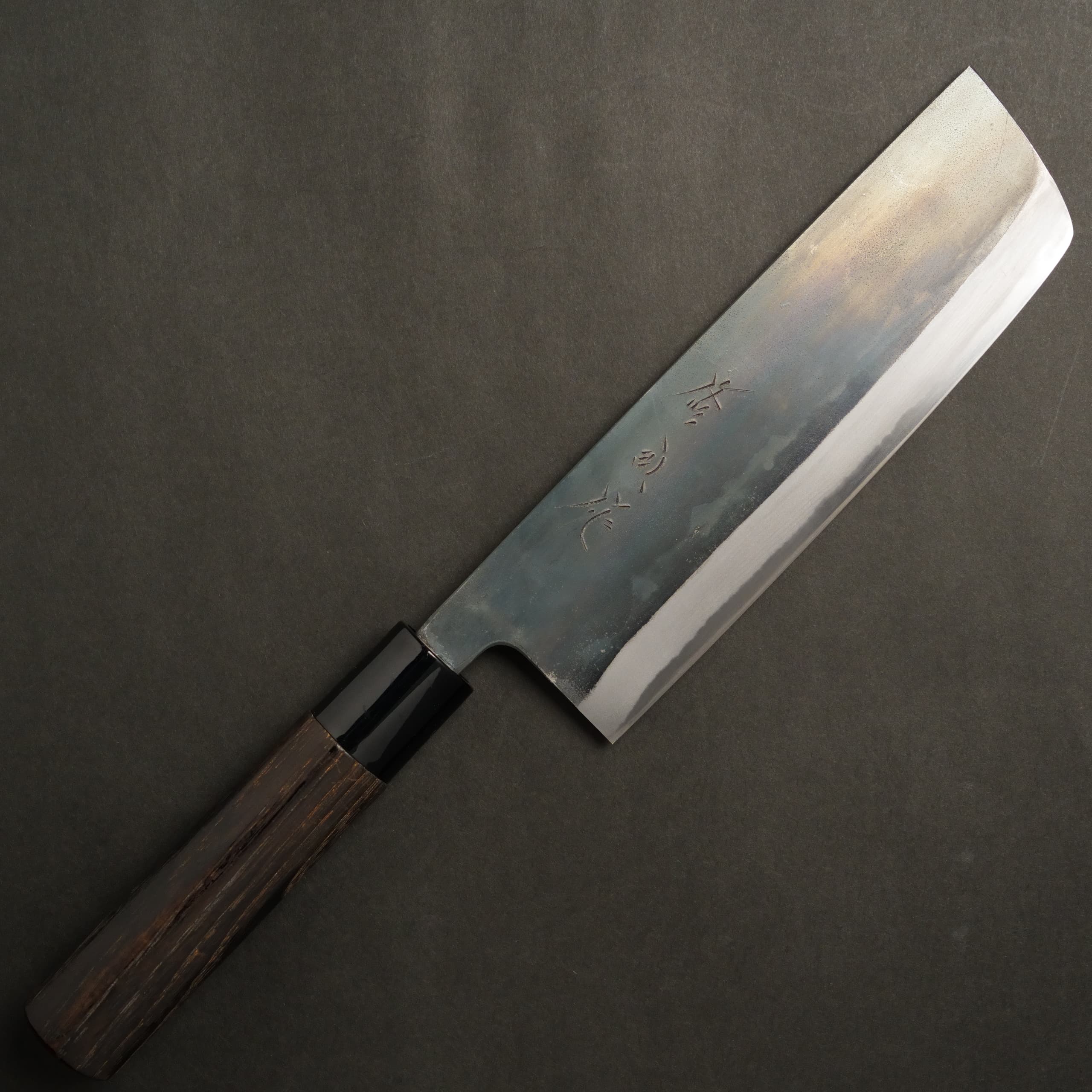Nakiri-style chef knife (165mm) with a dark/blackened blade and chestnut-style handle laid on a dark background.