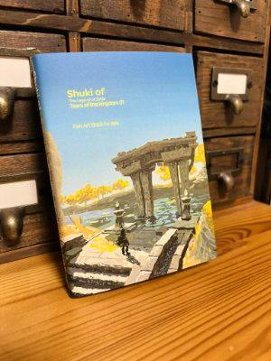 Front cover of the illustration book 'Shuki of Tears of the kingdom 01 : ハイラル語' propped on a wooden surface, showing artwork of a stone structure over water and a small silhouetted figure.