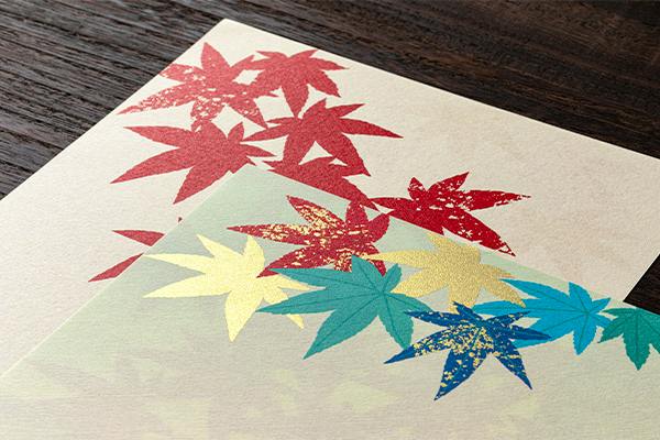 Two sheets of letter paper showing a colorful maple-leaf pattern on a wooden surface.