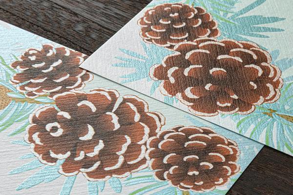 Close-up of letter pad sheets showing a printed pinecone wreath pattern on textured paper.