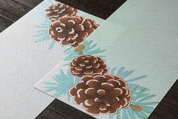 Letter pad sheets with a printed pinecone wreath design on textured paper.