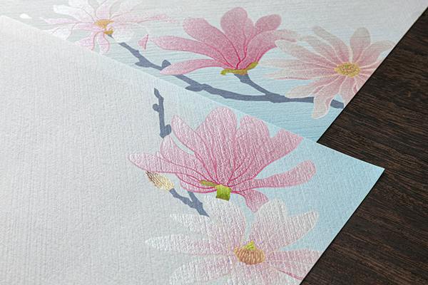 Two sheets of textured letter paper showing a pink magnolia-style floral pattern on a dark wood surface.