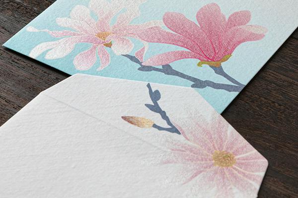 Close-up photo of silk envelopes showing a pink しでこぶし floral pattern on light blue and white backgrounds.