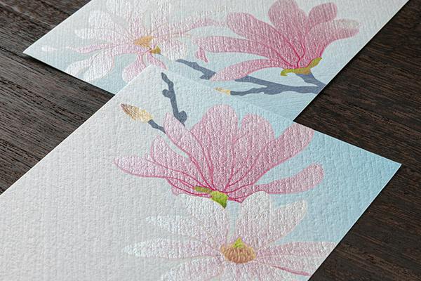 Two textured sheets of letter paper with a pink shide-kobushi (magnolia) floral pattern on a dark wooden surface.