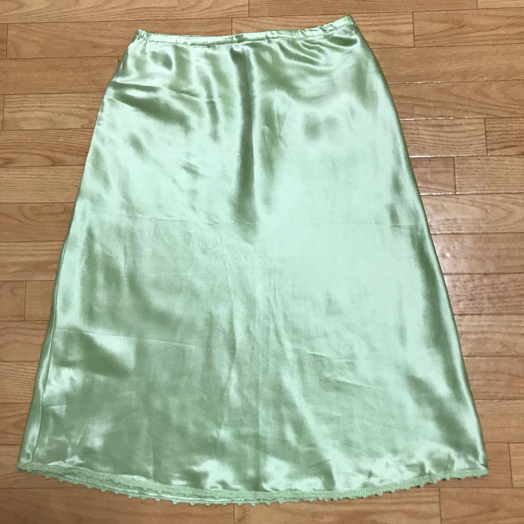 Light green silk women's skirt laid flat on a wooden floor.