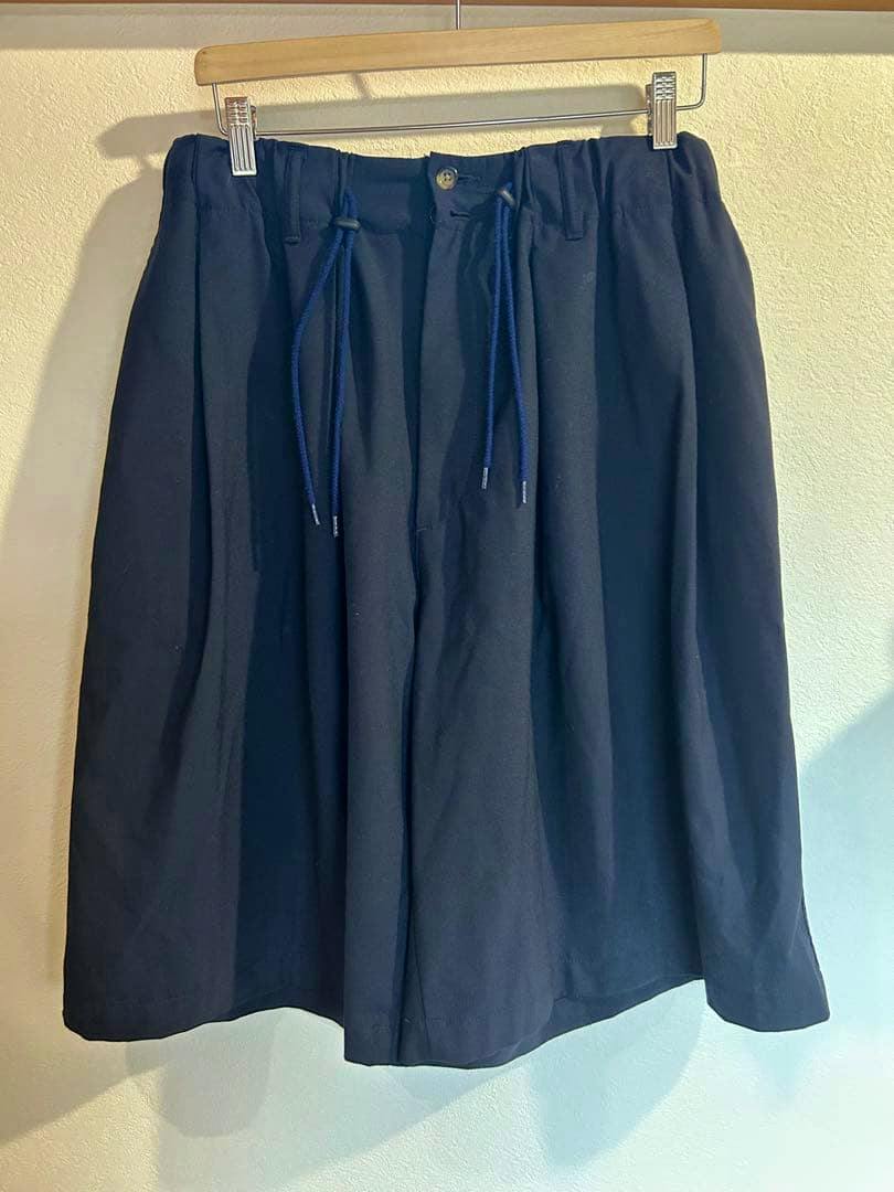 Front view of navy cotton Sillage circular short pants hanging on a wooden hanger with visible drawstring and button.