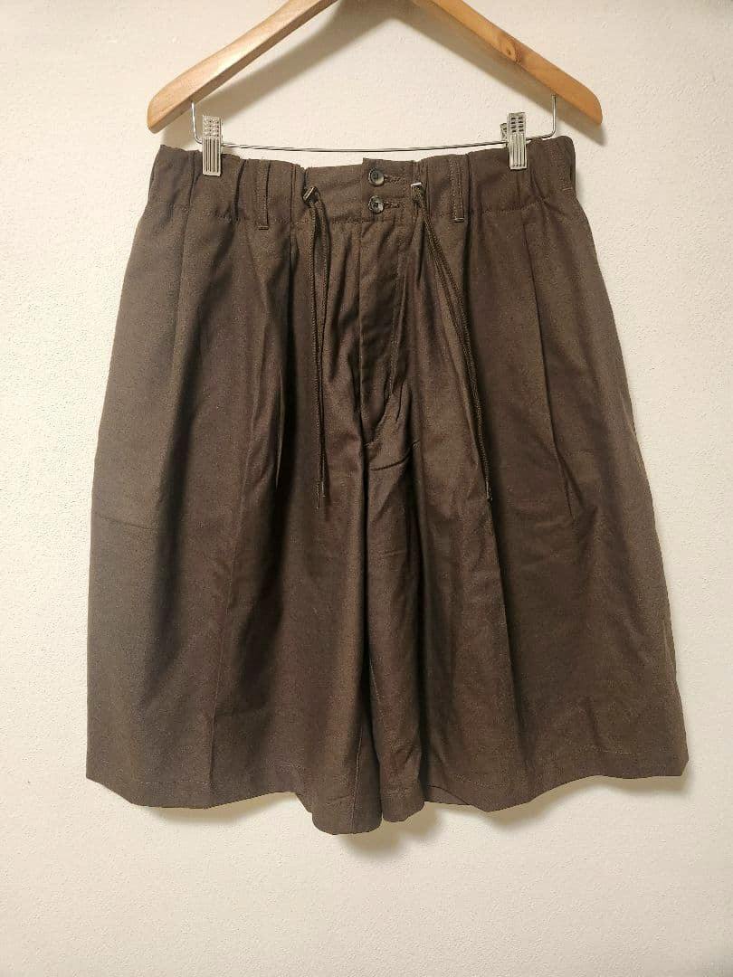 Brown Sillage circular men's shorts hanging on a wooden hanger against a light wall.