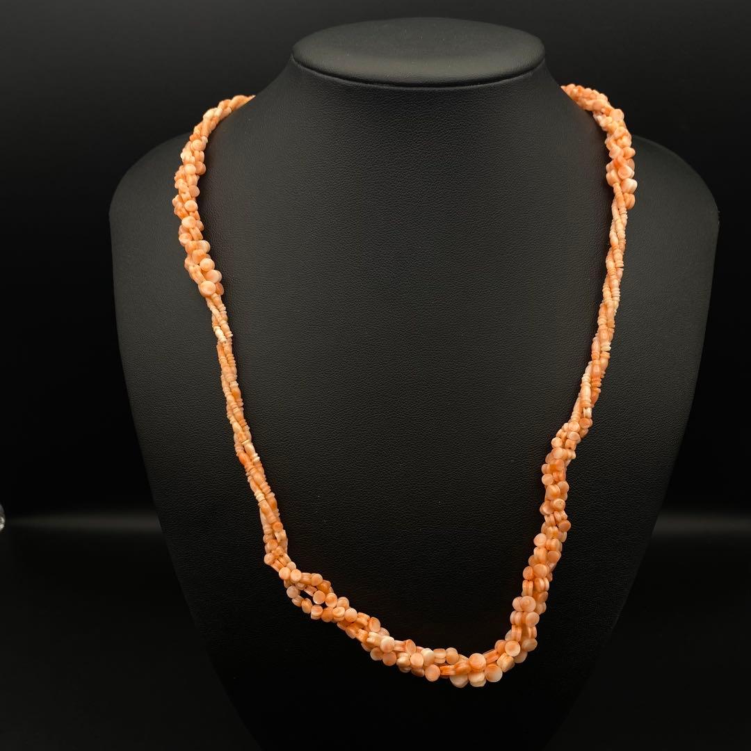 Pinkish coral-bead necklace with twisted strands displayed on a black jewelry bust.