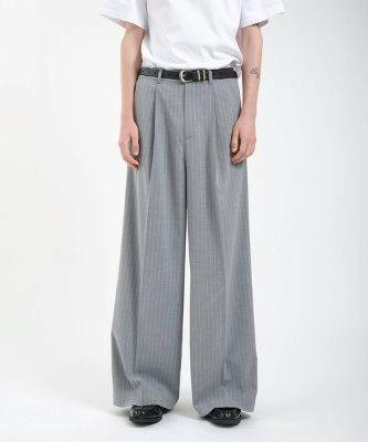 Front view of a model wearing gray single-pleat buggy slacks with wide legs and a black belt.