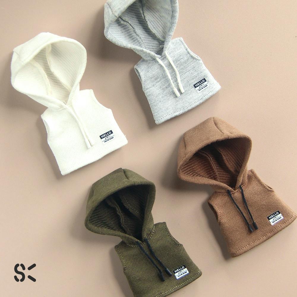 Four sleeveless hooded doll sweaters in white, gray, brown, and olive green laid flat on a beige background.