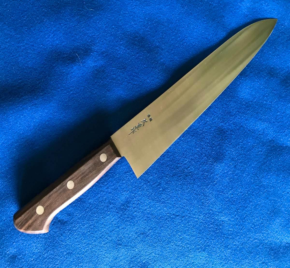 SK鋼牛刀270mm chef knife with a wooden handle lying on a blue fabric background, showing the blade and kanji markings.