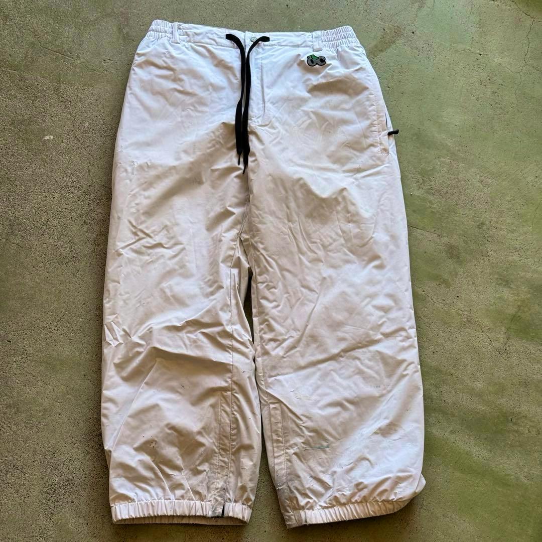 White ski/snowboard pants laid flat on the ground showing the front view.