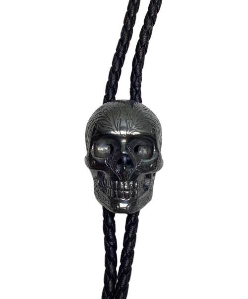 A silver skull pendant threaded on two braided black cords against a white background.