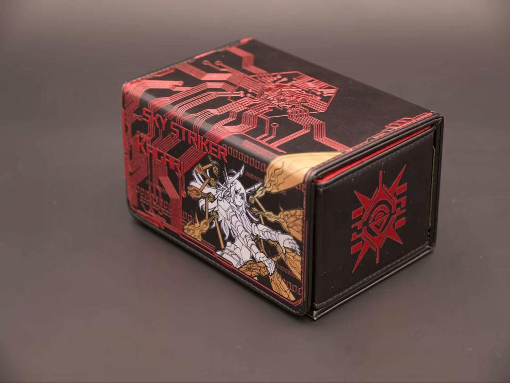 Angled photo of the 閃刀姫 deck case (polyester) showing a red circuit-pattern and white character illustration on a black background.