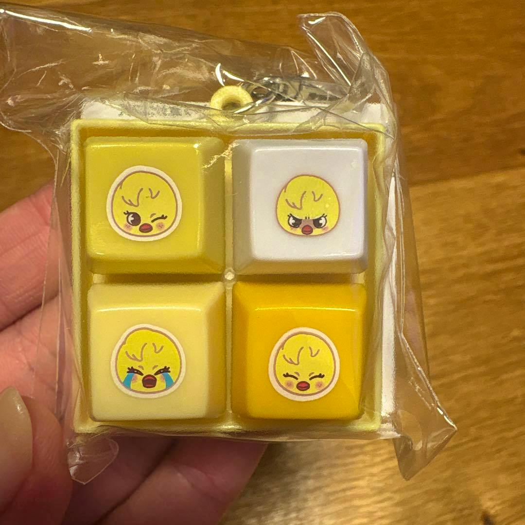 Plastic keychain with four yellow square blocks featuring chick face stickers shown in clear packaging held by a hand.