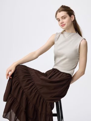 A model seated on a stool wearing the sleeveless bottle-neck cotton T-shirt.