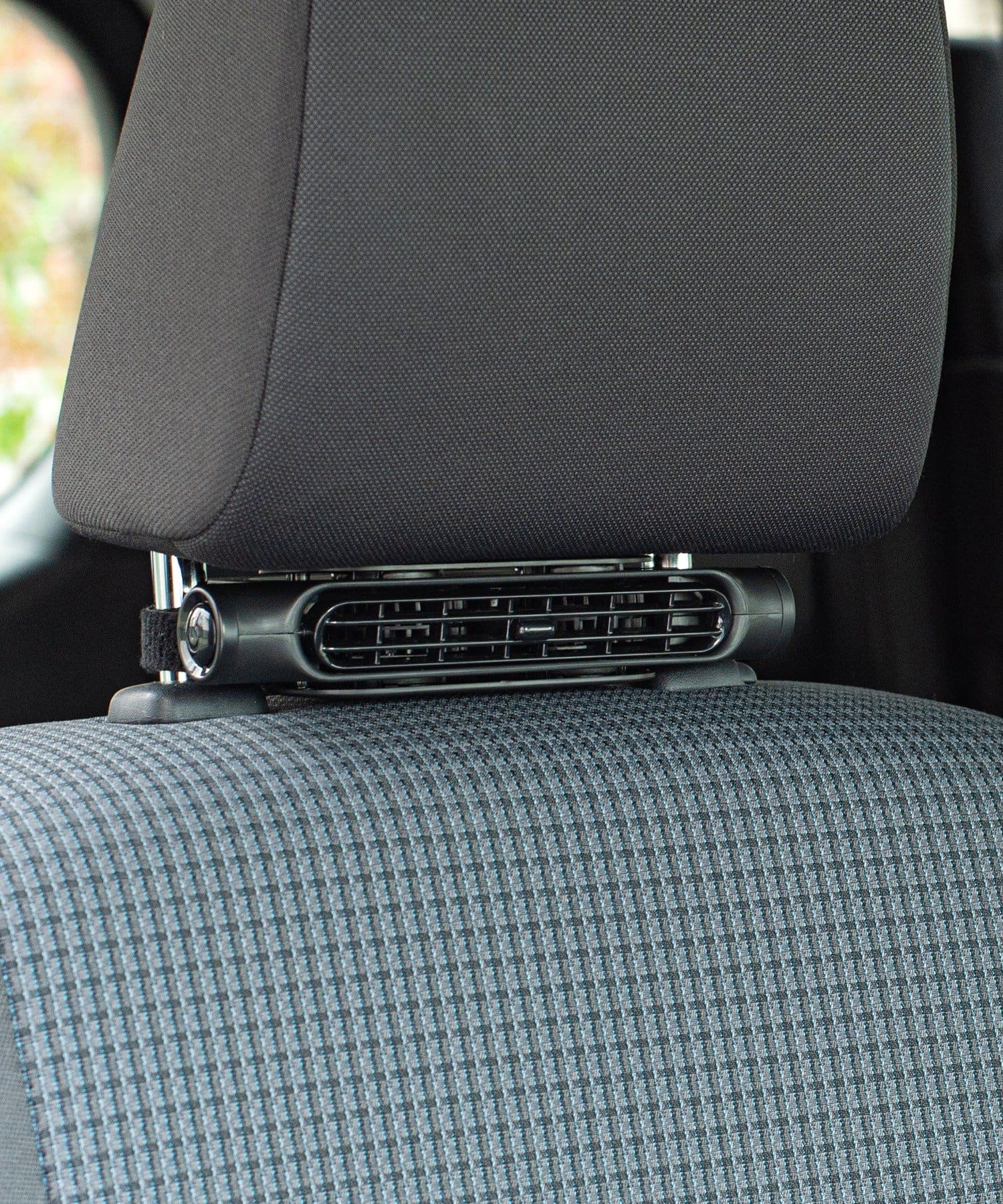 A slim fan attached to a car headrest above a fabric car seat.