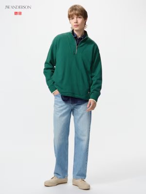 Male model standing against a white background wearing light-blue slim-straight men's jeans and a green pullover.